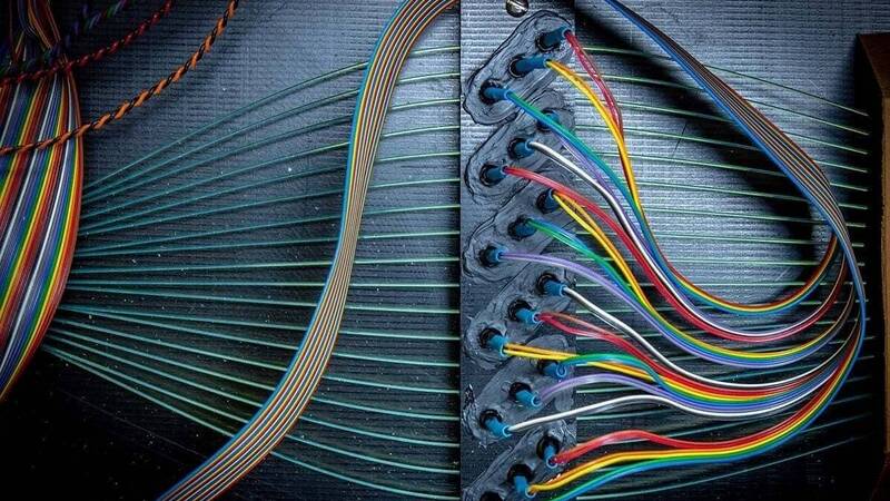 Vibrant red, blue, yellow, and green wires are plugged into a dark panel with blue connectors, next to a rainbow-colored ribbon cable.