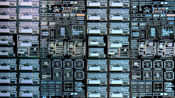 The image shows a detailed view of a silicon wafer with blue and white microchip circuits (small squares and rectangles) and a small Notre Dame leprechaun logo.