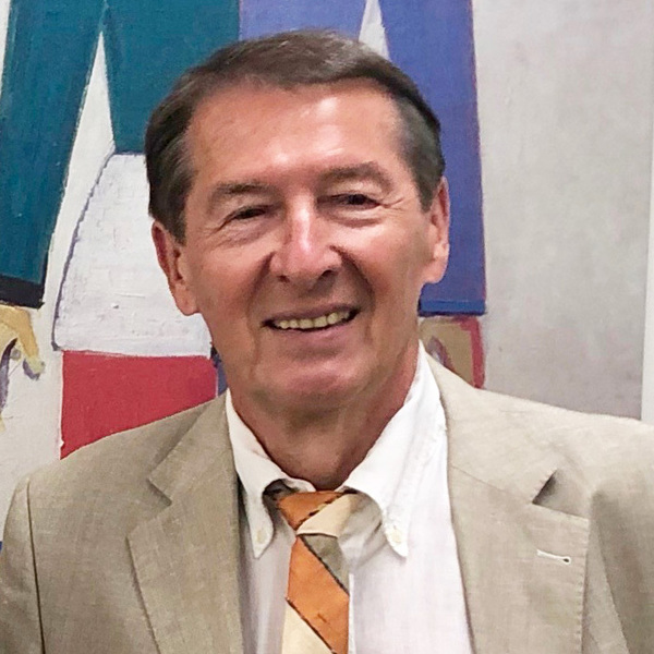 Smiling man in a beige suit jacket, white shirt, and orange, cream, brown striped tie. Abstract background.
